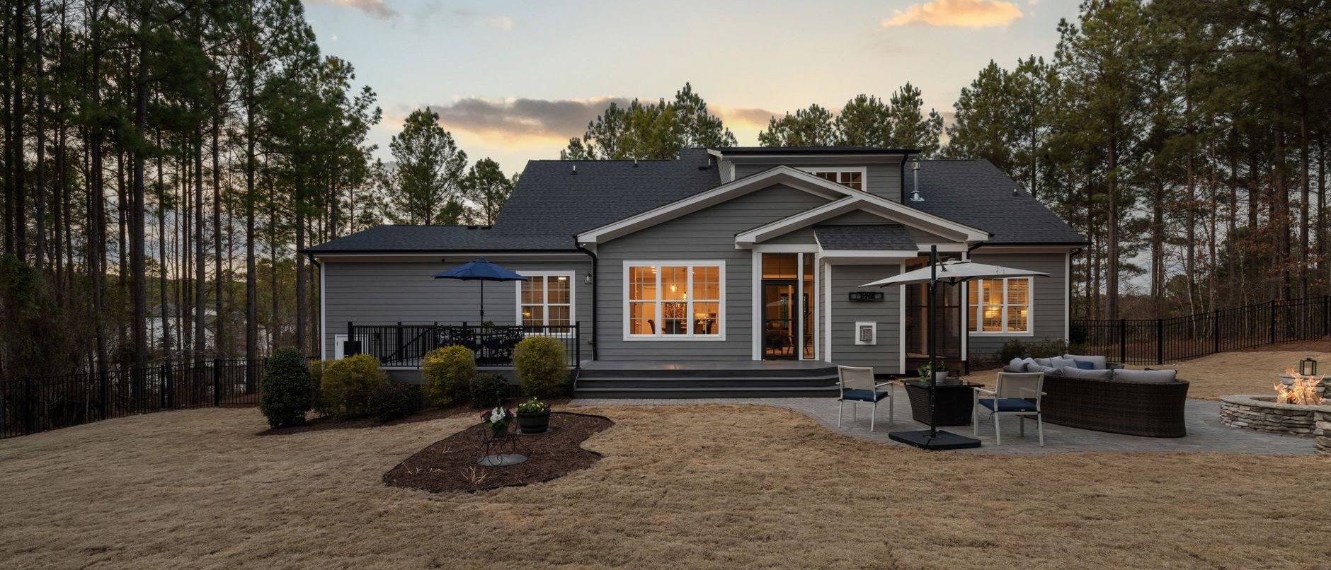 A low house at dusk with a lit deck and landscaping