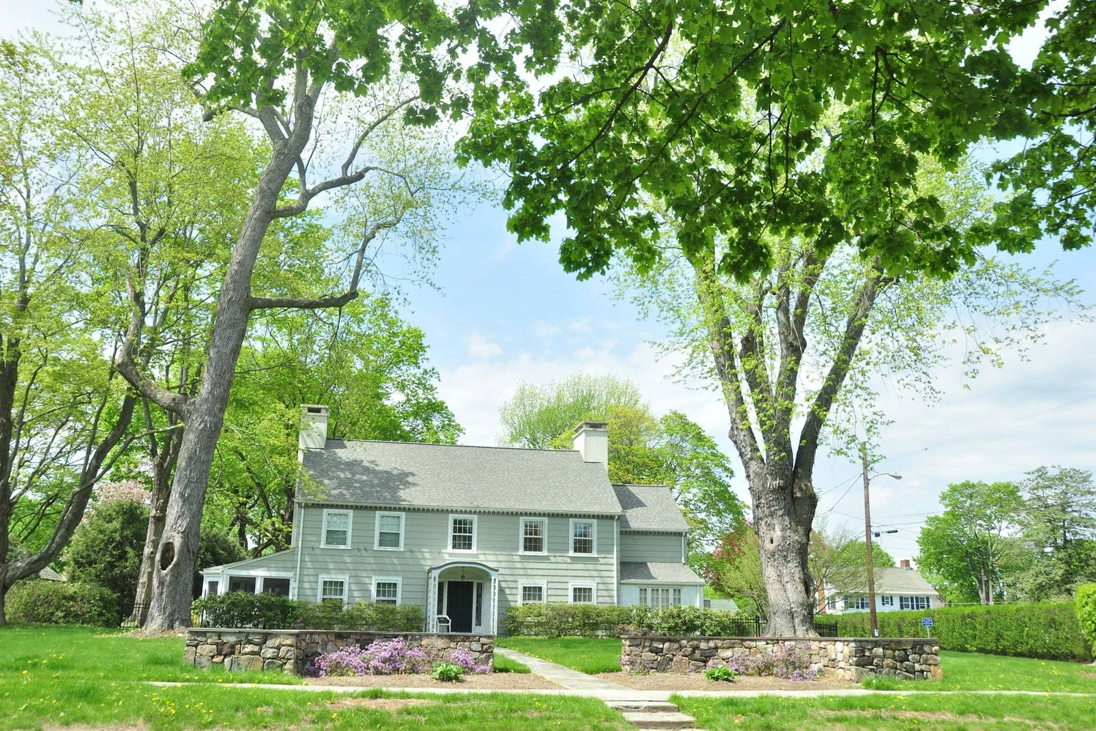 A 1920s center-hall colonial on a large lot under mature maples, with a fieldstone wall along the sidewalk