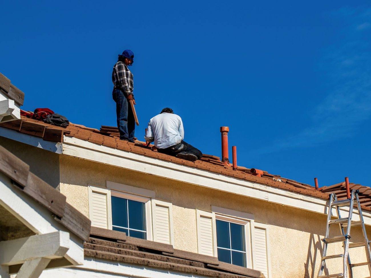 A roofer working on a residential roof with a ladder against the eaves