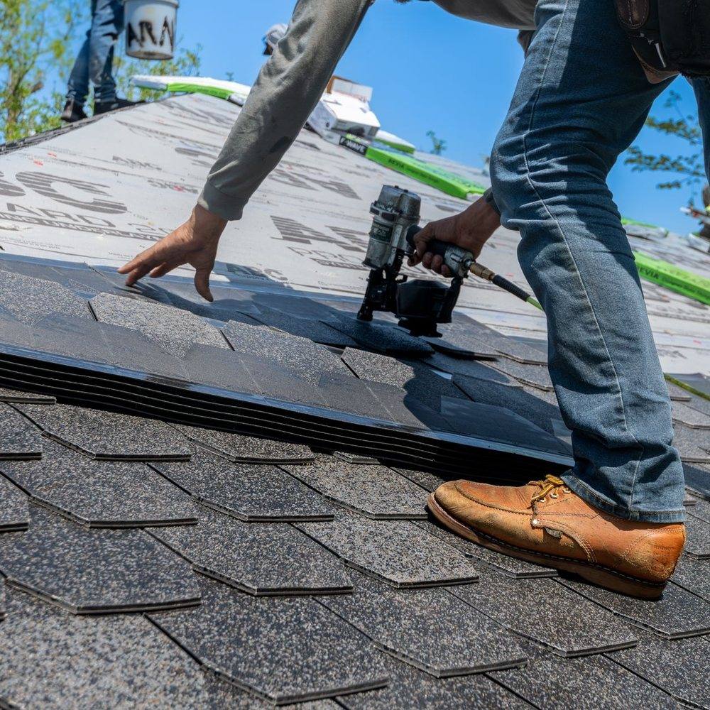 A roofer nailing a course of architectural shingle, working across a stripped and re-laid section