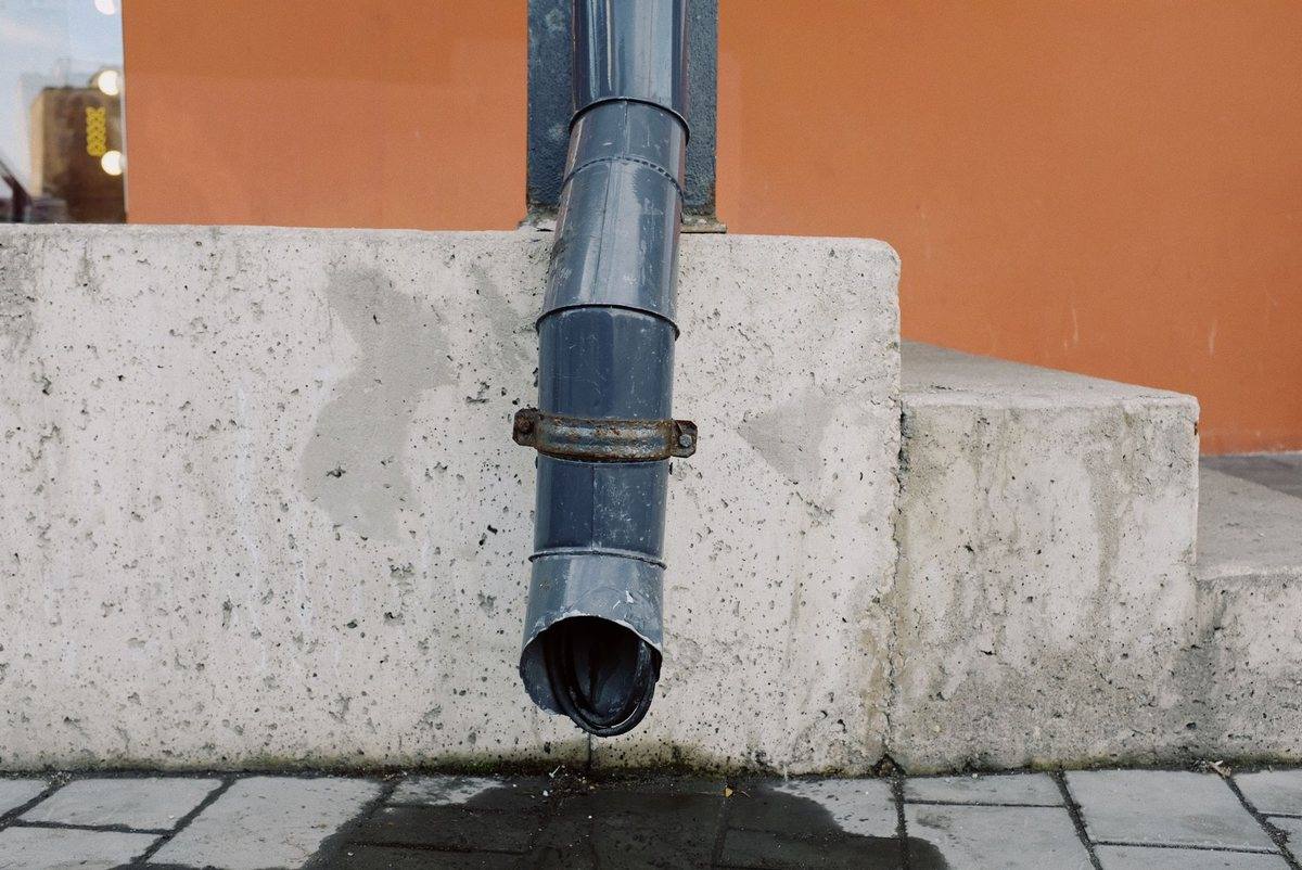 A downspout discharging rainwater onto paving beside a wall