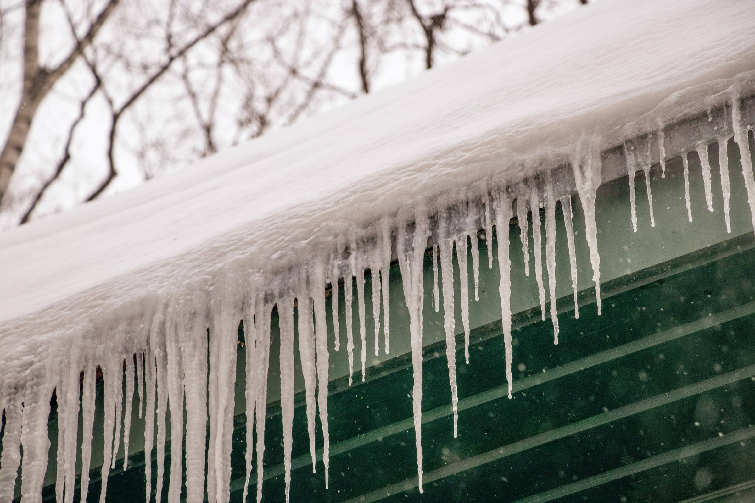 Snow loaded along a roof edge, with a row of icicles hanging over the siding below