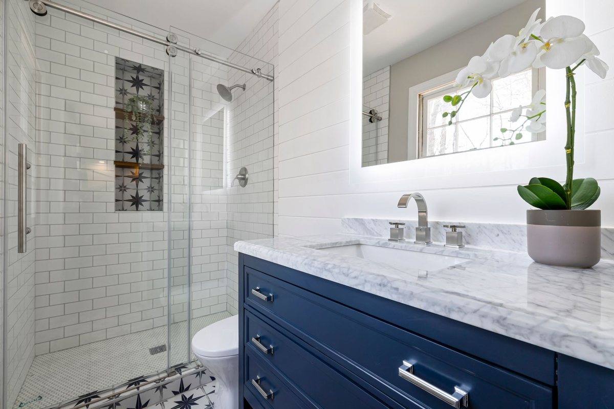 A navy vanity with marble top and a glass shower