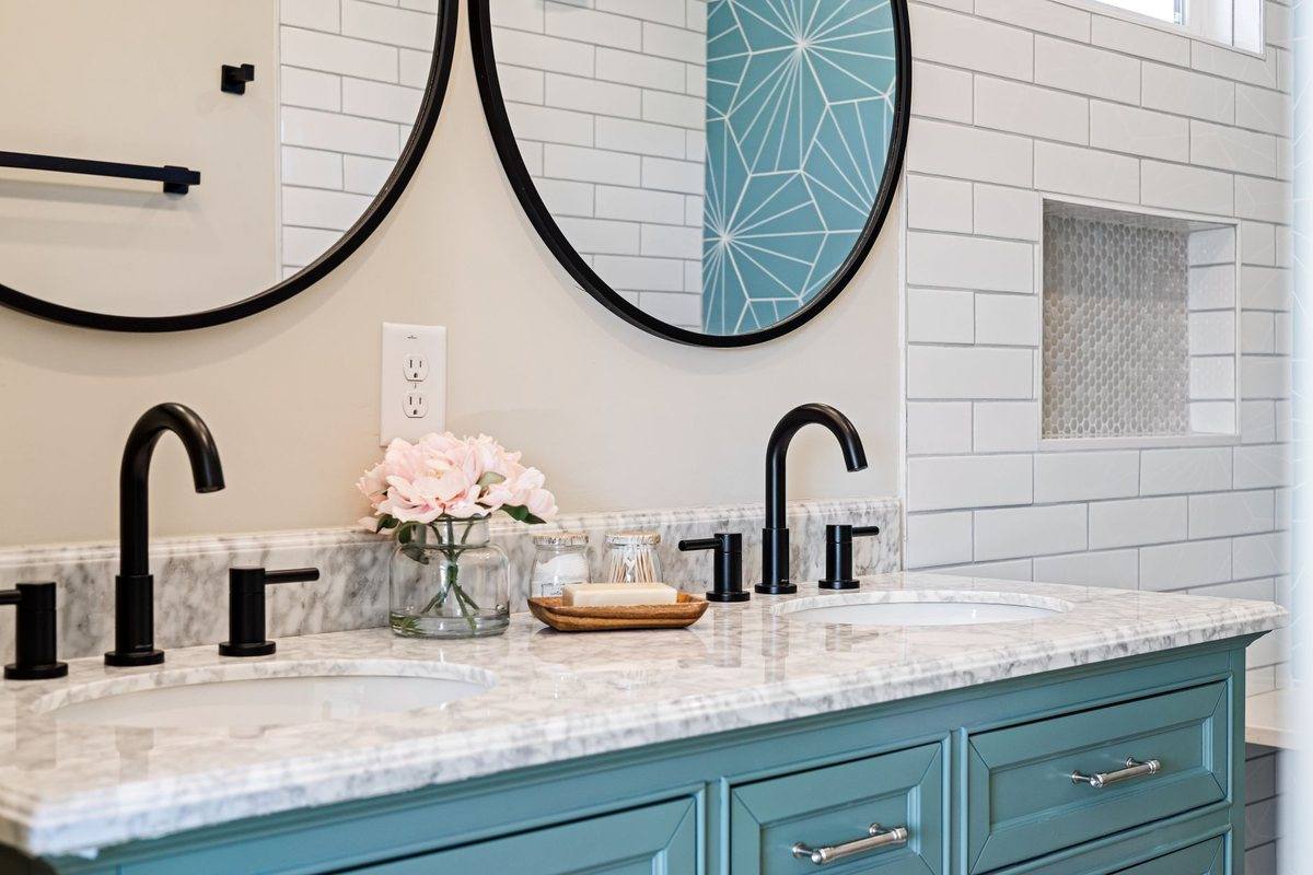 A bathroom with a teal vanity and two round mirrors