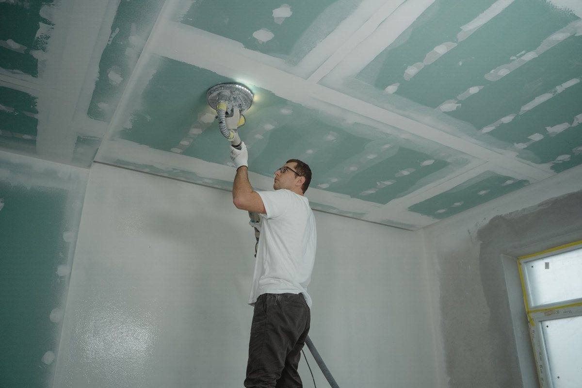 A tradesman finishing drywall on a ceiling during a renovation