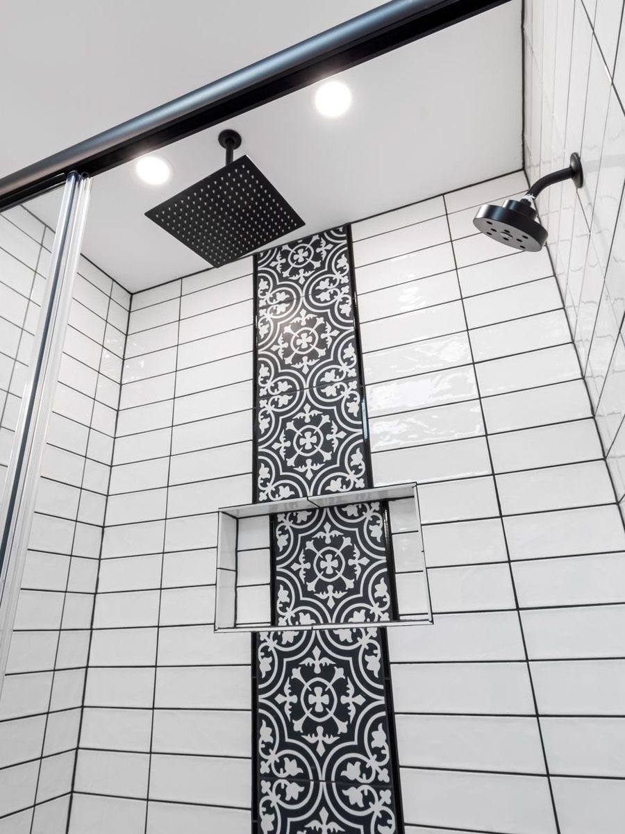 A tiled shower wall with a vertical mosaic band and black fittings