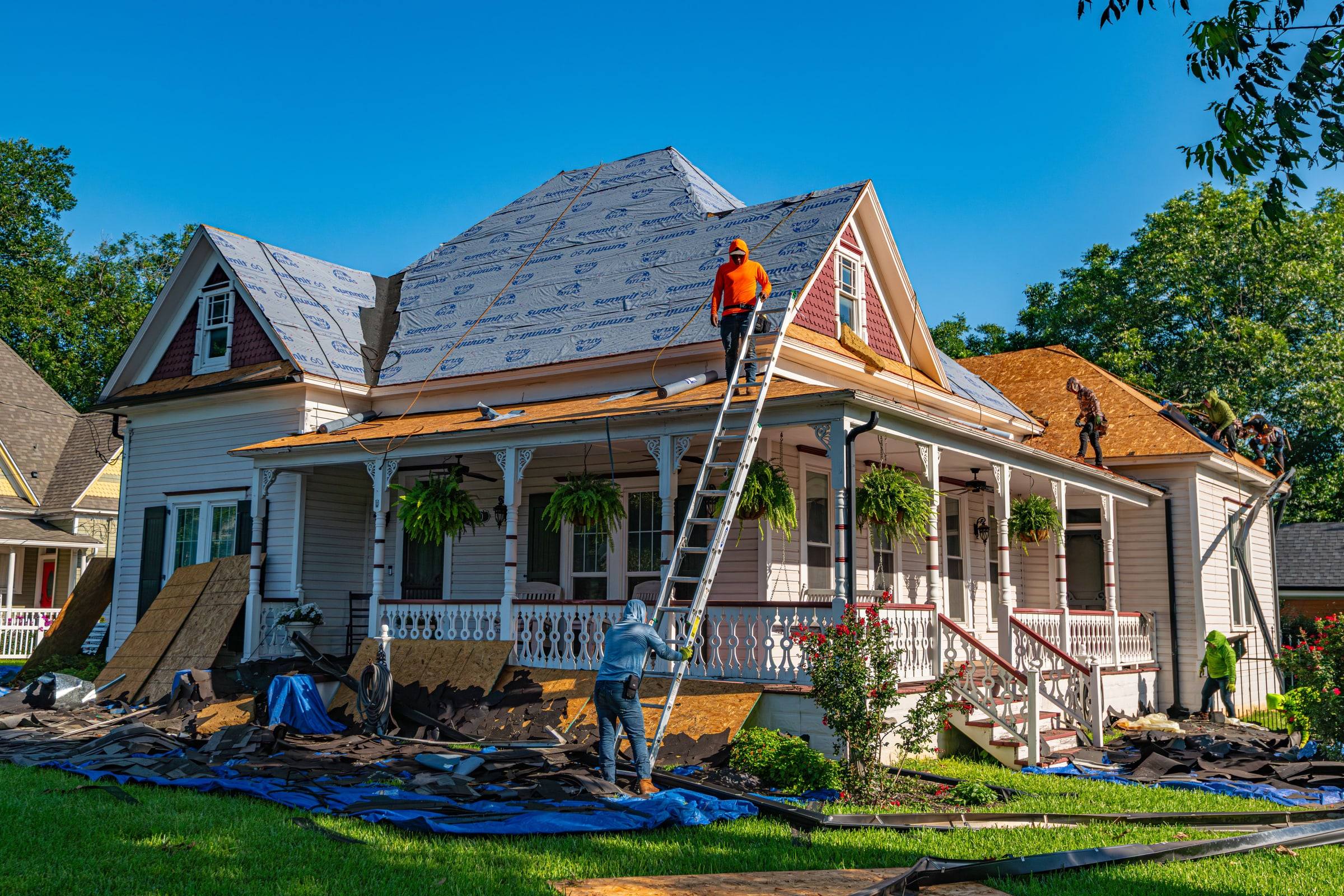 A roofing crew at work on a house with the ladder up and the roof opened