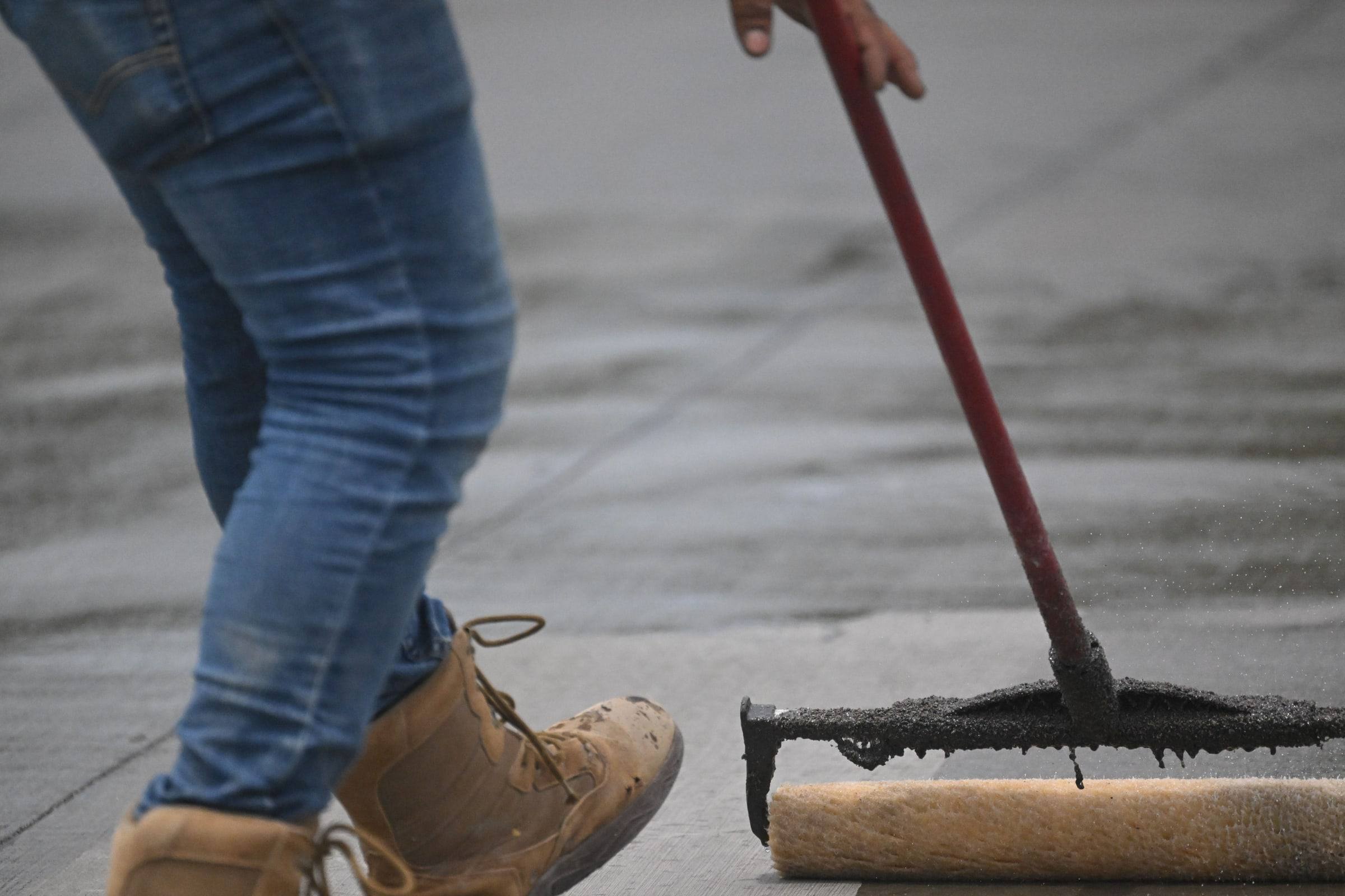 A roofer working a coating across a low-slope roof with a long-handled squeegee
