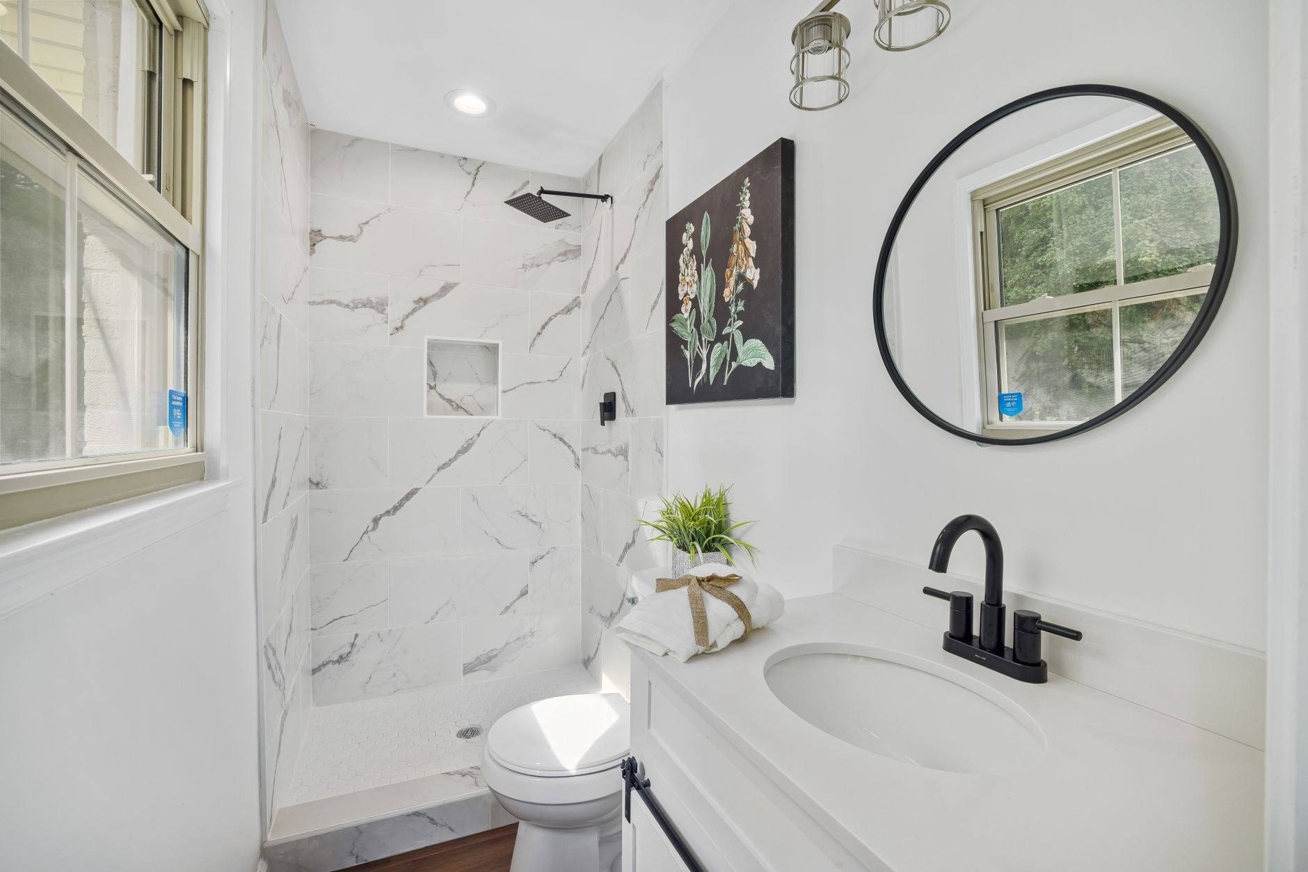 A bright bathroom with marble tiling, a round mirror and black fittings