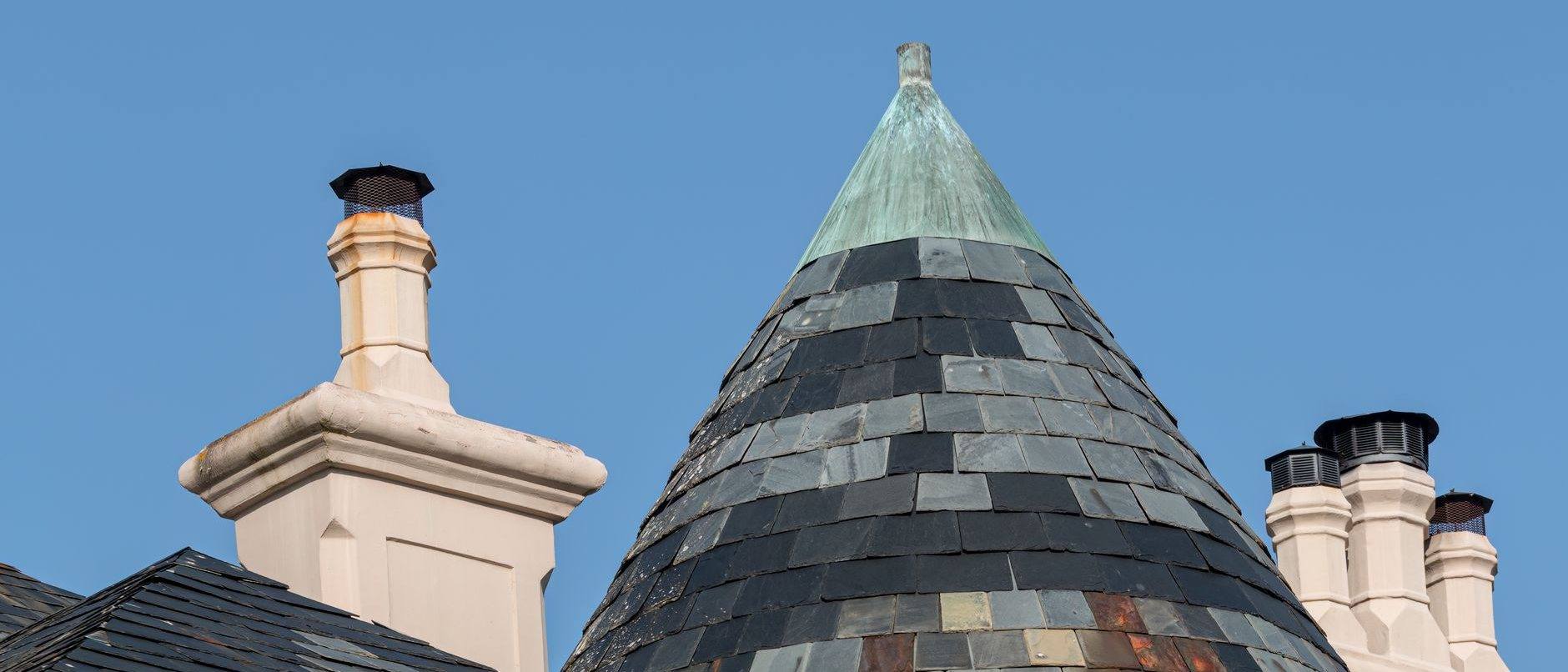 A slate-clad turret and brick chimneys against a clear sky