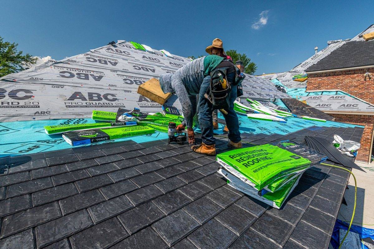 A roofer rolling out synthetic underlayment across a roof deck