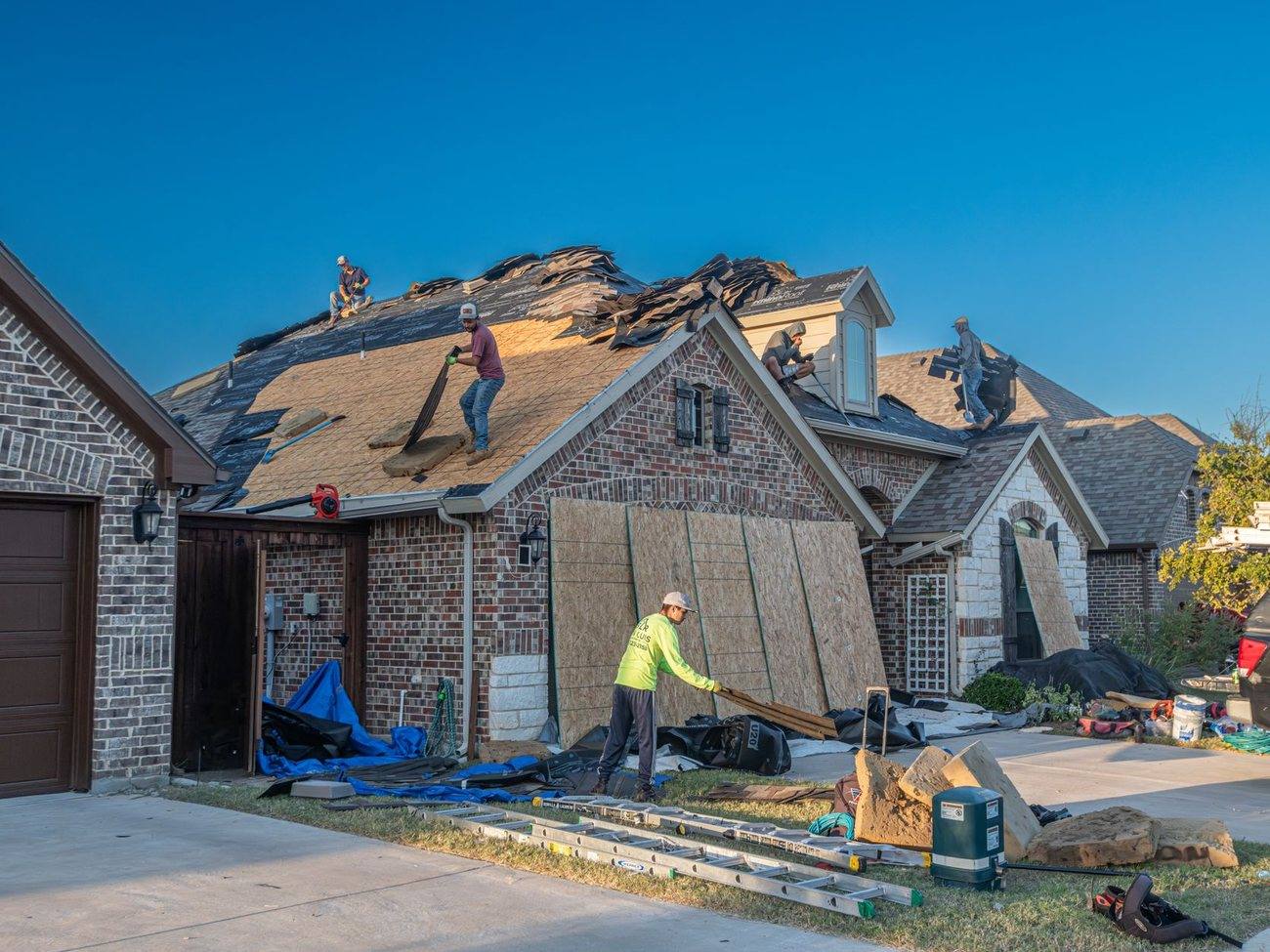 A crew re-roofing a large stone and shingle house