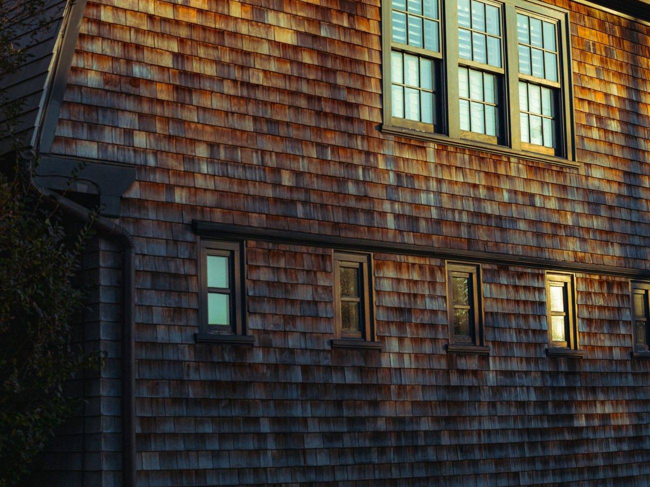 A cedar shingle house with a lit window at dusk