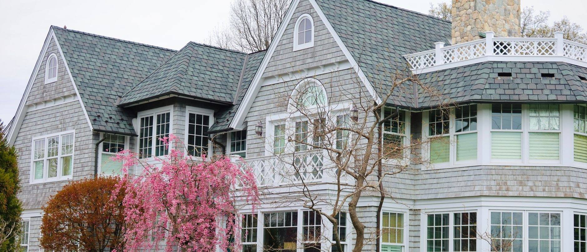 A gray shingled house with white trim behind a flowering cherry tree