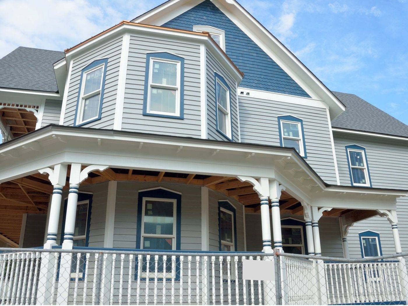 A pale blue clapboard Victorian house with a wraparound porch