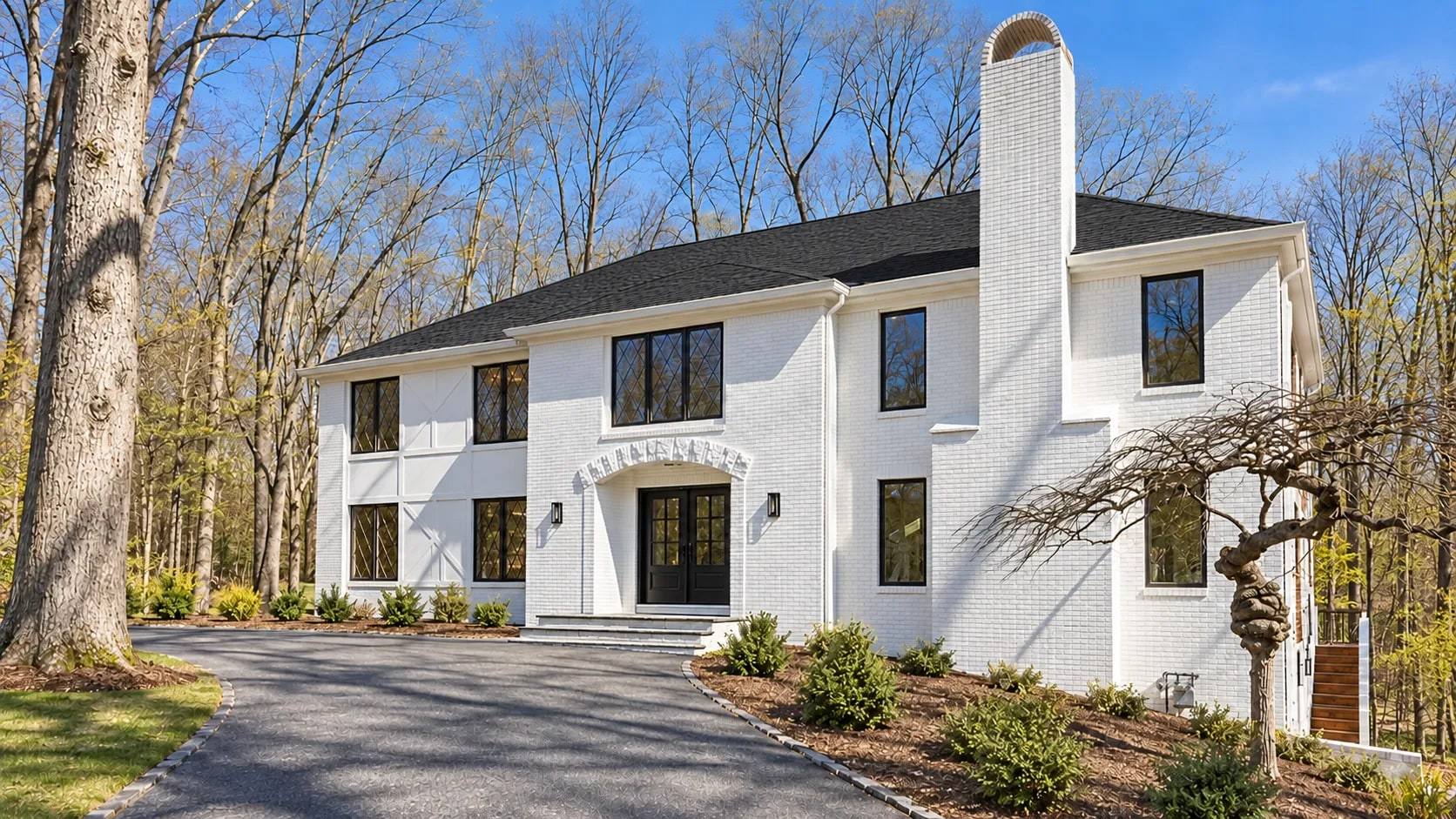 A white-painted brick house with black-framed windows, leaded diamond-pane casements and black double entry doors under an arched brick surround