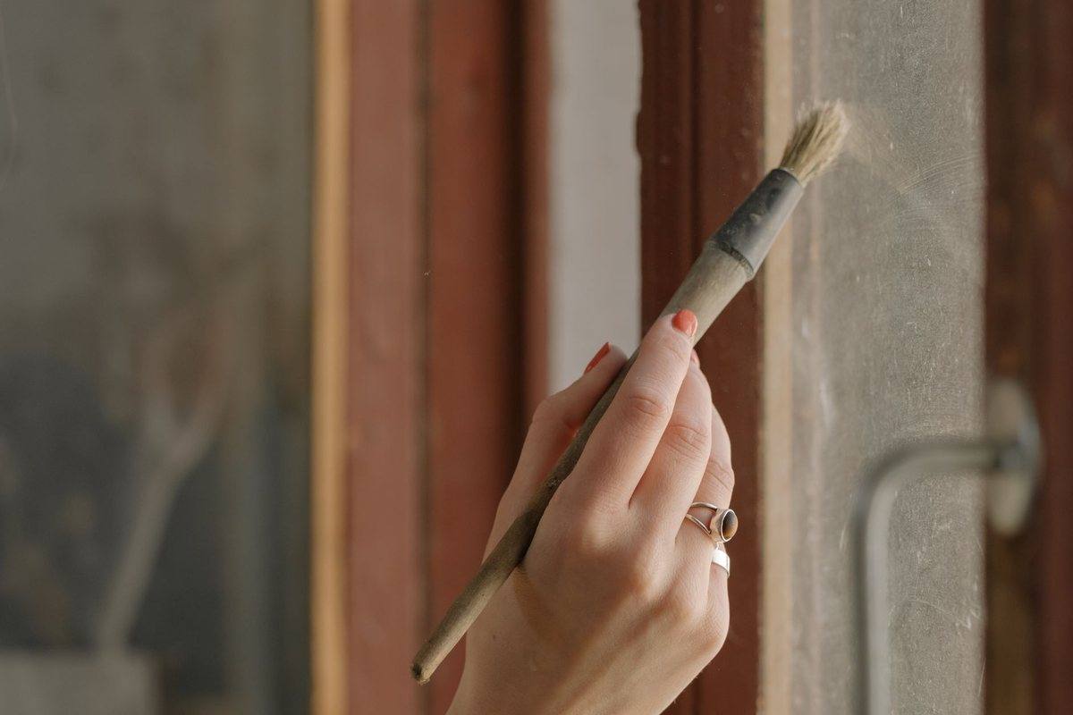 A hand painting the frame of a wooden window with a brush