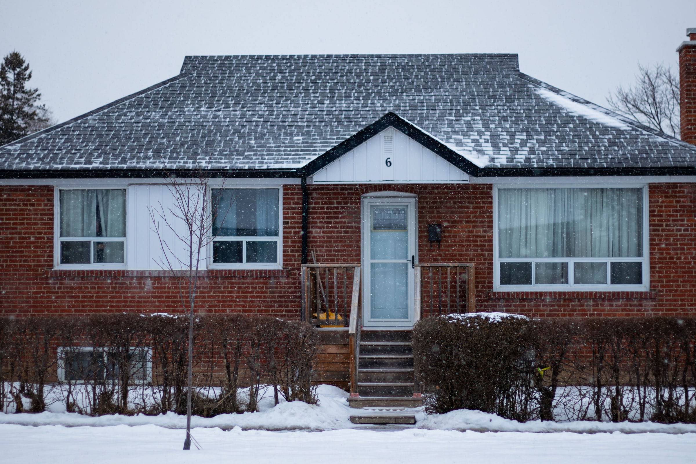 A brick bungalow with frost on its gray shingle roof and snow along the front walk