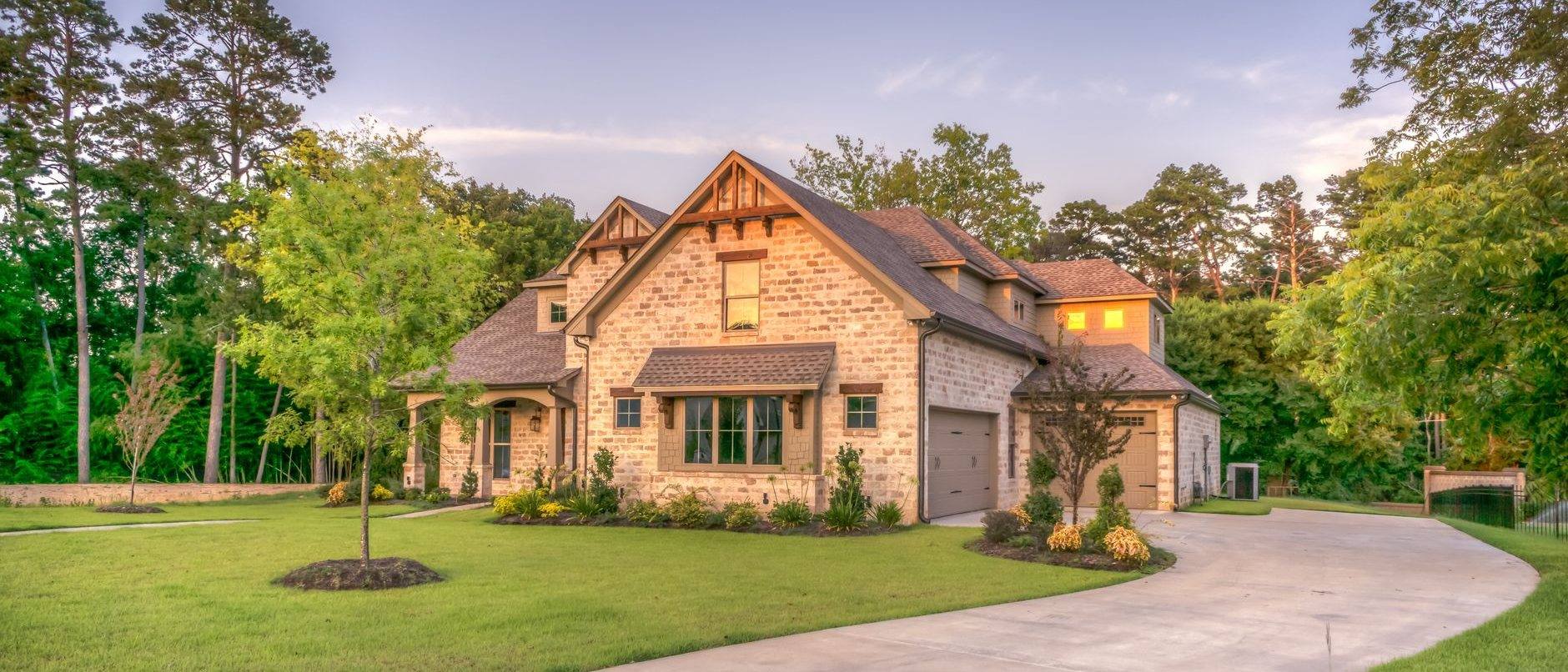 A large stone and shingle house at dusk with a curved driveway